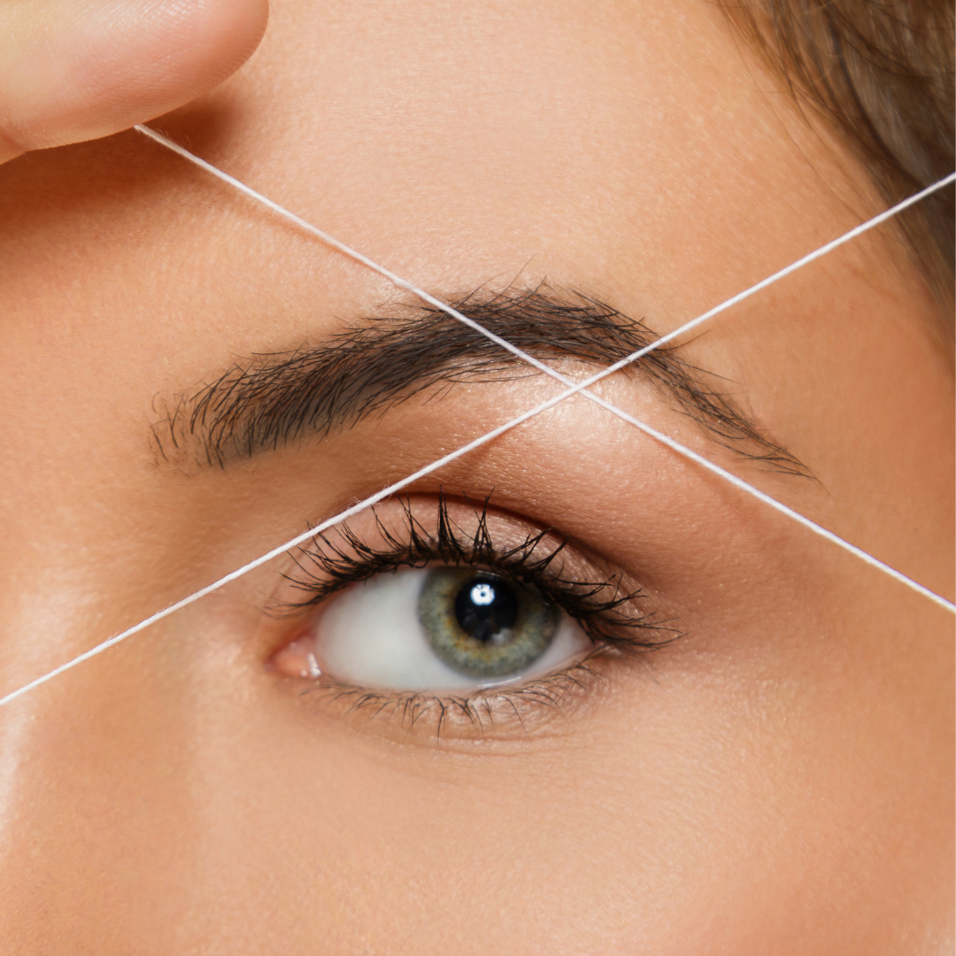 Een close-up foto van een oog waarbij de wenkbrauwen worden ge-thread, een precieze techniek voor het verwijderen van overtollige haartjes rond de wenkbrauwlijn