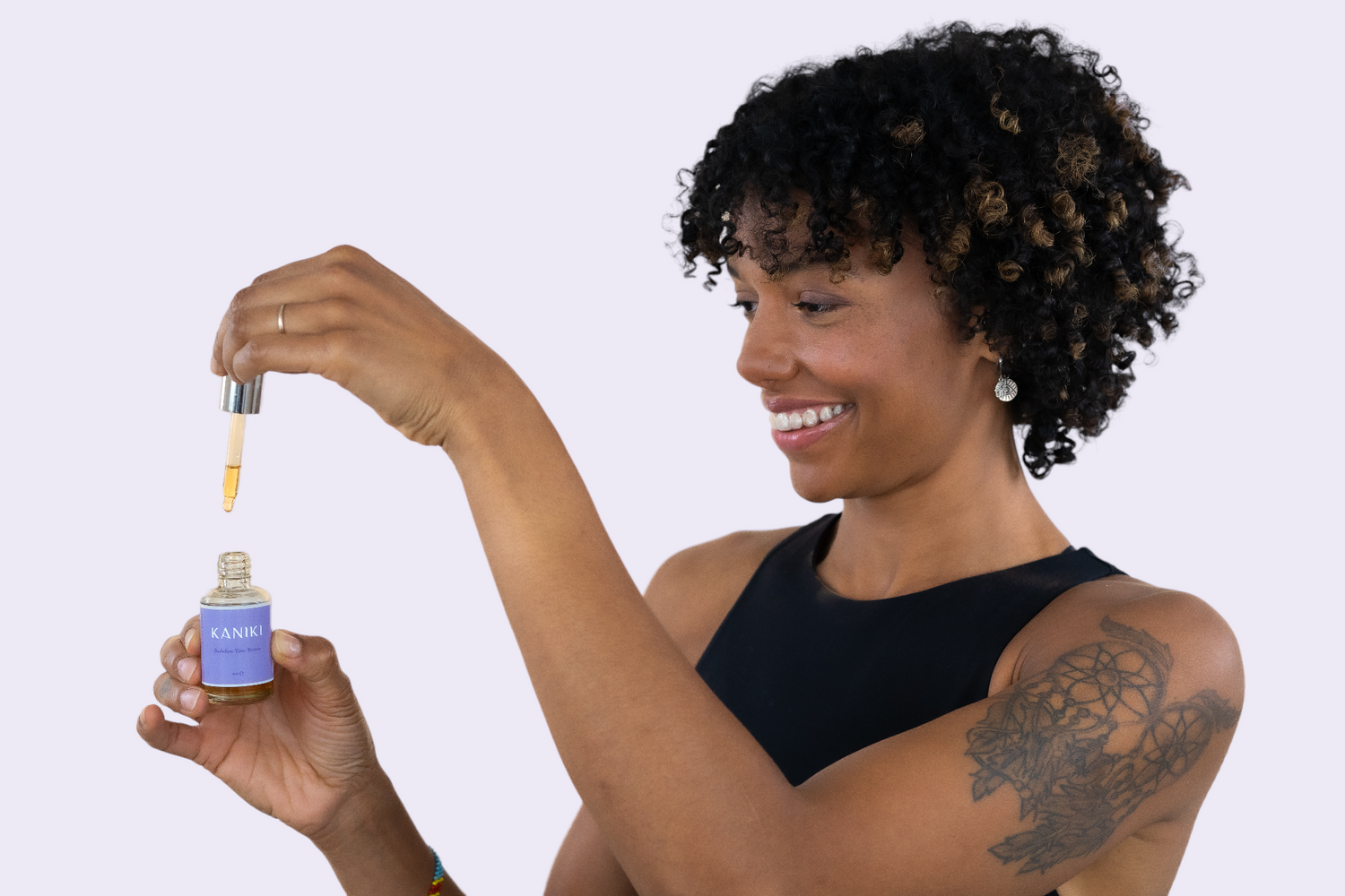 Foto van een vrouw die het Kaniki Elixir voor wenkbrauwen flesje vasthoudt in haar ene hand, terwijl ze met haar andere hand het pipetje toont, waarmee het product nauwkeurig kan worden gedoseerd, wat de gebruiksvriendelijkheid benadrukt.