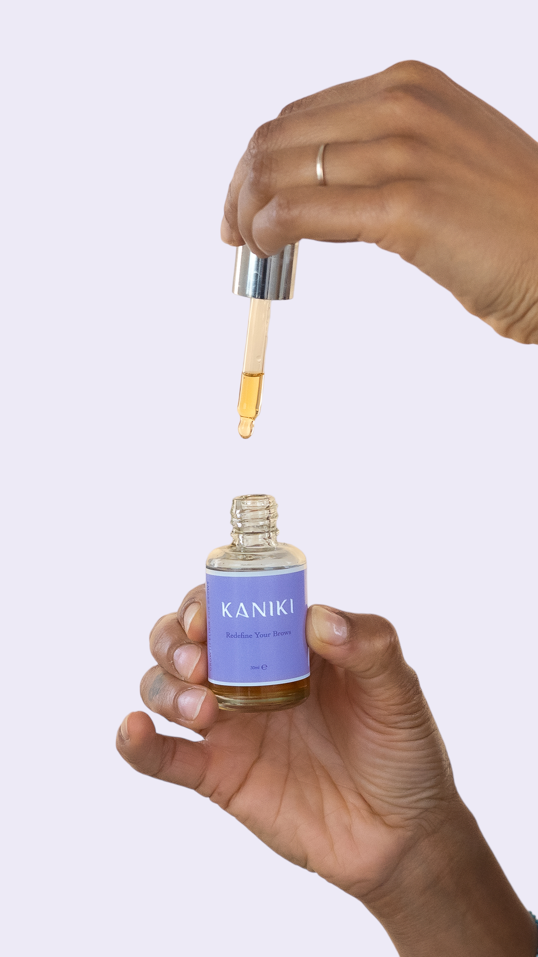 Foto van een hand die het Kaniki Elixir voor wenkbrauwen flesje vasthoudt in de ene hand, terwijl ze met de andere hand het pipetje omhoog houdt, klaar voor precieze dosering en toepassing.